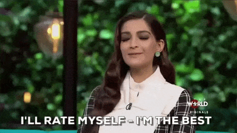 Confident woman smiling and saying "I'll rate myself – I'm the best" during a TV interview on a lush, green set.